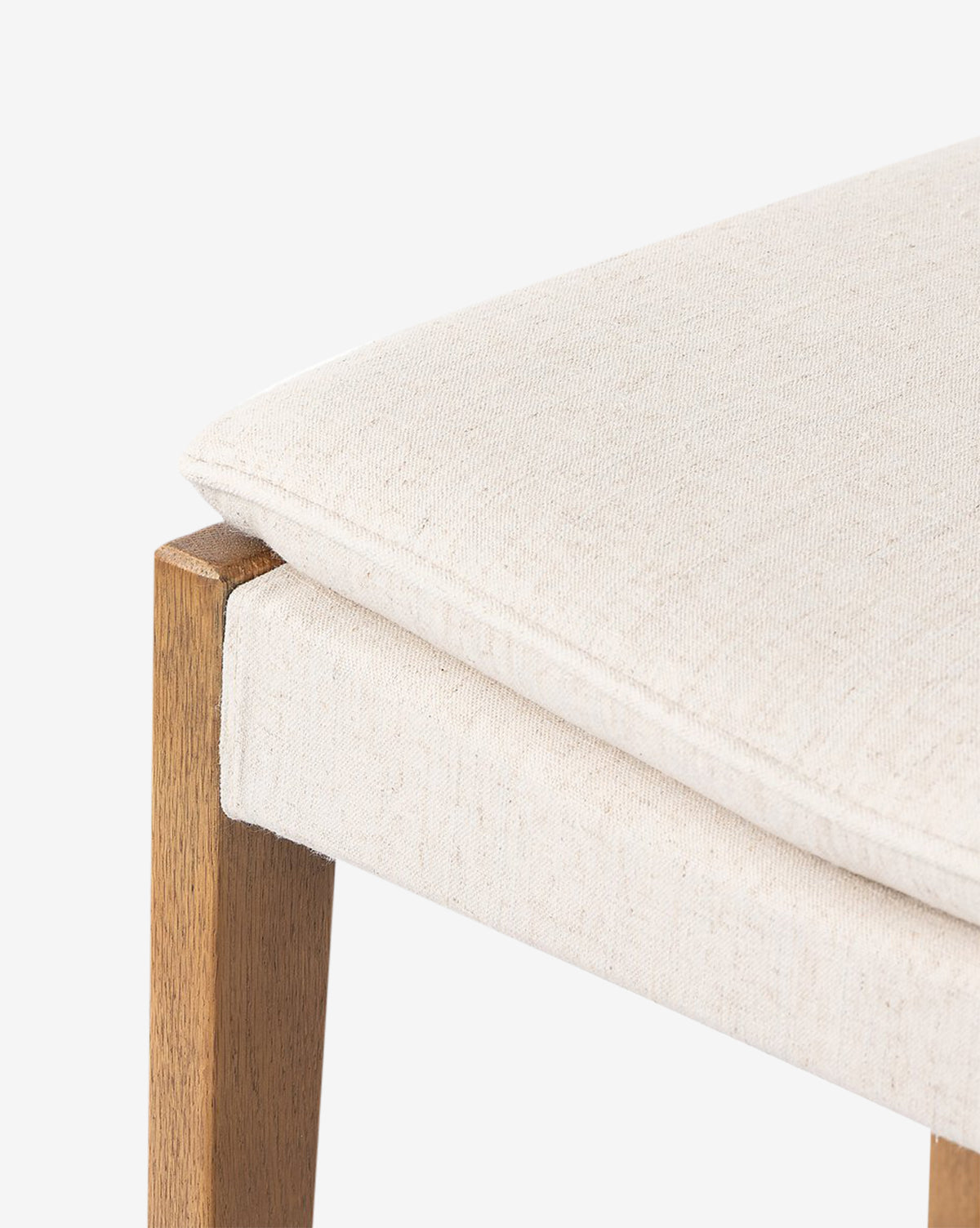Close-up of the Four Hands Kaelith Counter Stool, showcasing its light beige upholstered seat and solid oak legs against a plain white background. McGee & Co.