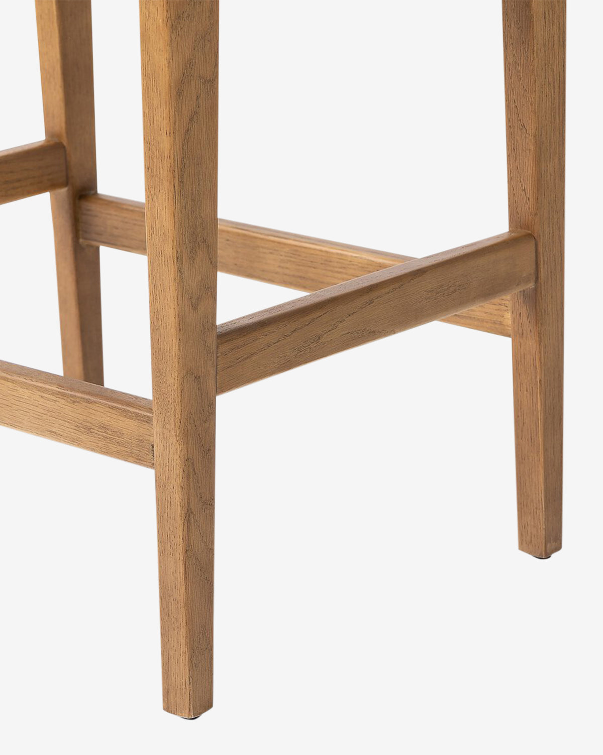 Close-up of the lower legs and footrest of the Four Hands Kaelith Counter Stool, highlighting its natural wood grain and light brown solid oak finish against a white background. McGee & Co.
