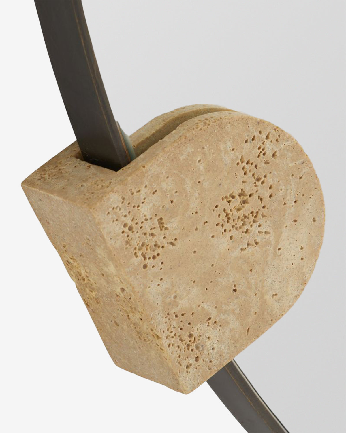 The Kairos Mirror features a close-up of its textured faux travertine block, set against a curved, bronze-plated steel frame on a plain light background, by McGee & Co.