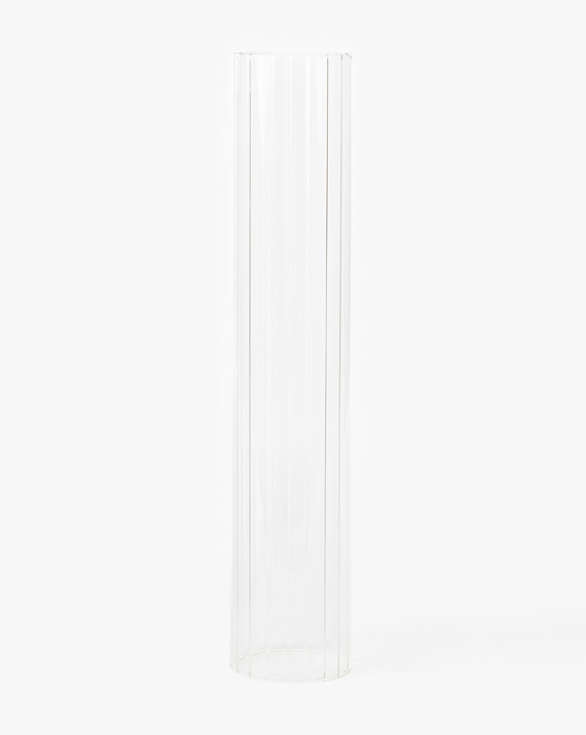 The Kalina Ribbed Candle Sleeve is a tall, clear, cylindrical glass holder with subtle vertical ridges, resembling an elegant taper candle holder. It stands upright against a plain white background.