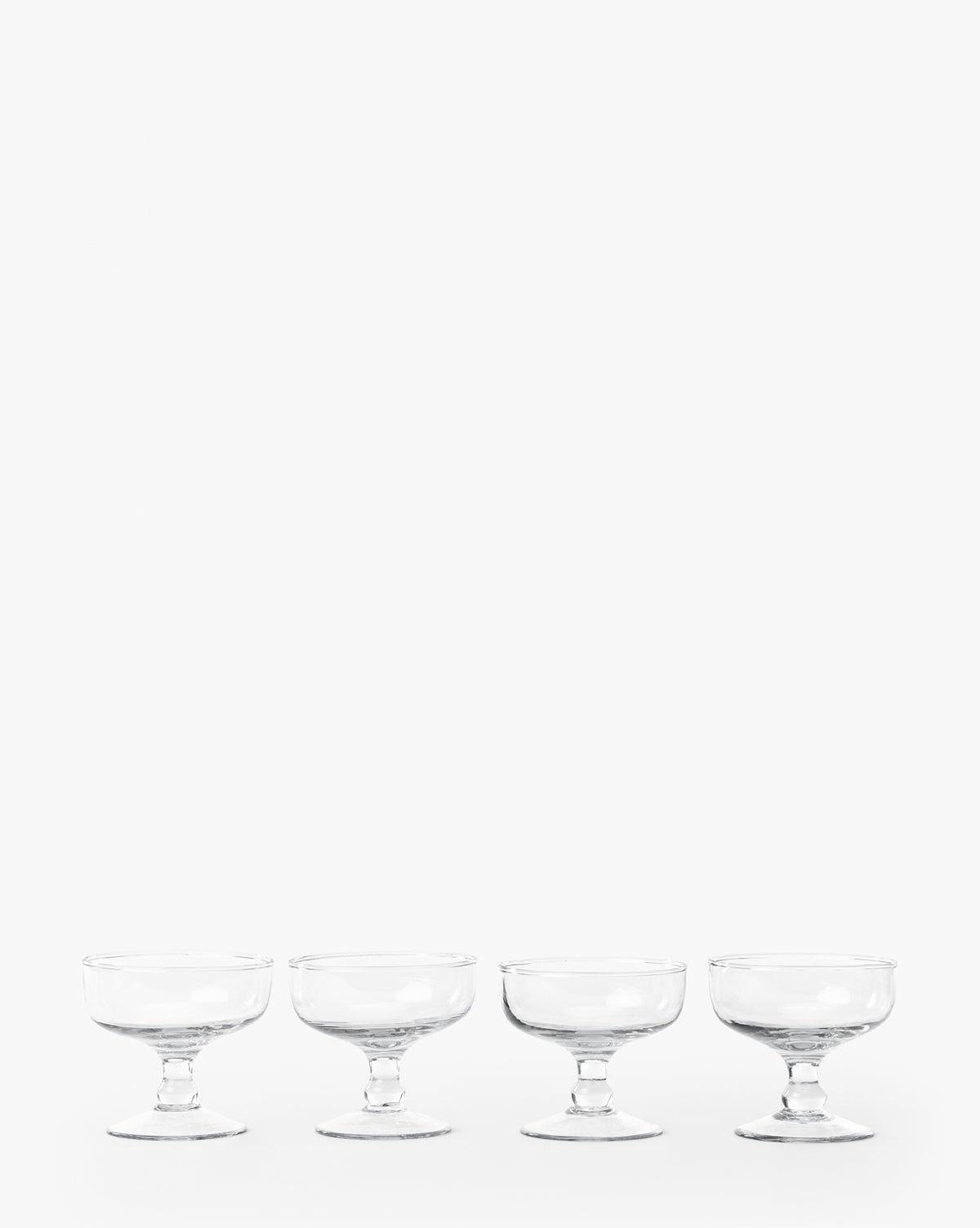 The Keely Coupe (Set of 4) features four clear coupe glasses neatly lined up in a row against a plain white background, by McGee & Co.