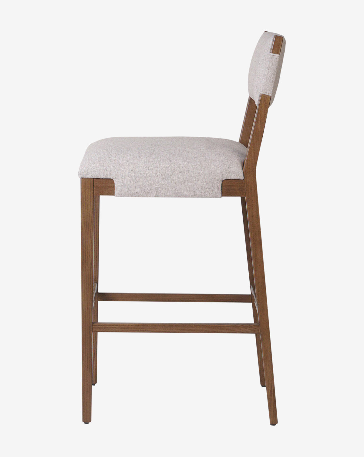 The Kennebec Stool by Four Hands features a side view of a modern design with a light beige performance fabric-upholstered seat and backrest, supported by an ash wood frame and legs with horizontal support bars by McGee & Co.