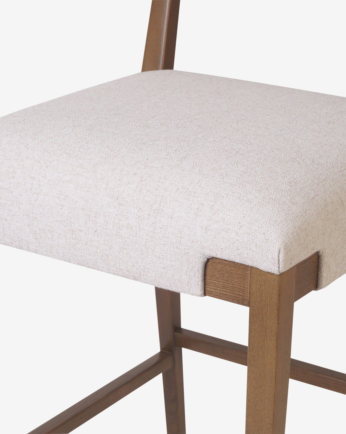 Close-up of the Four Hands Kennebec Stool, featuring a light beige performance fabric cushioned seat and ash wood frame, highlighting part of the backrest and legs against a plain white background. McGee & Co.