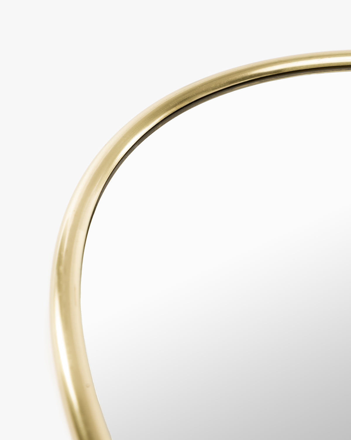 Close-up of the upper edge of a Kitson Oval Mirror featuring a thin, antique brass frame against a white background. The mirror’s surface looks clean and slightly reflective, by McGee & Co.