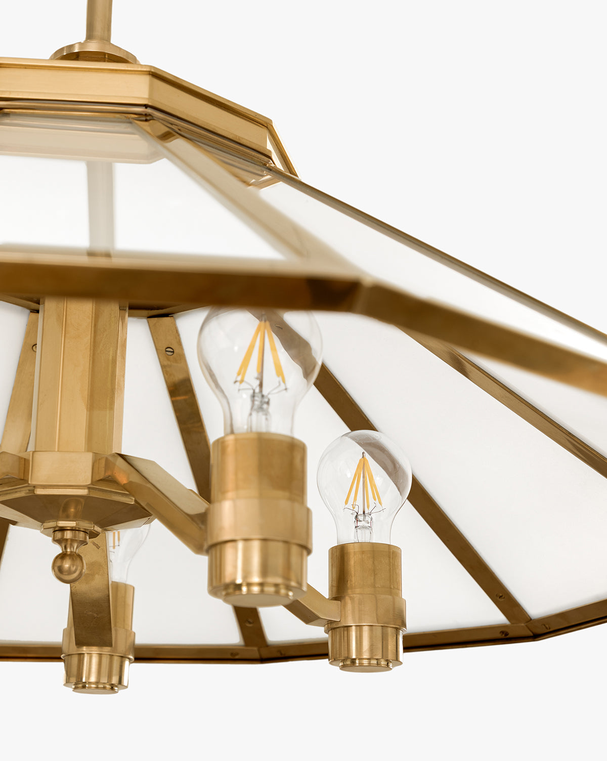 Close-up of the Knightley Chandelier in antique brass, featuring three exposed LED filament bulbs and a geometric glass shade against a light background, by McGee & Co.