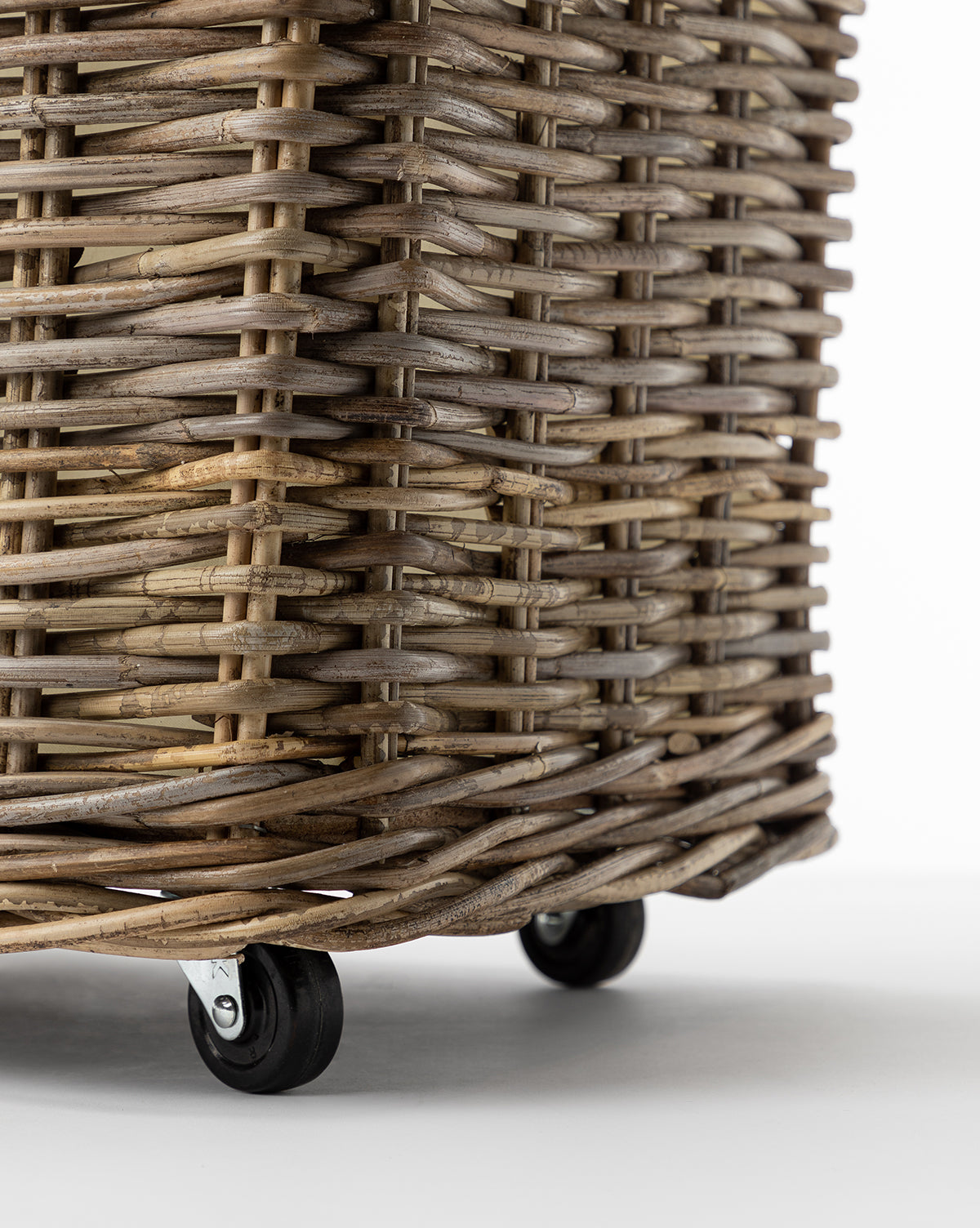 Close-up of the Kobo Wheeled Basket, a rectangular rattan laundry basket with a natural woven texture and small black caster wheels, set against a plain white background.