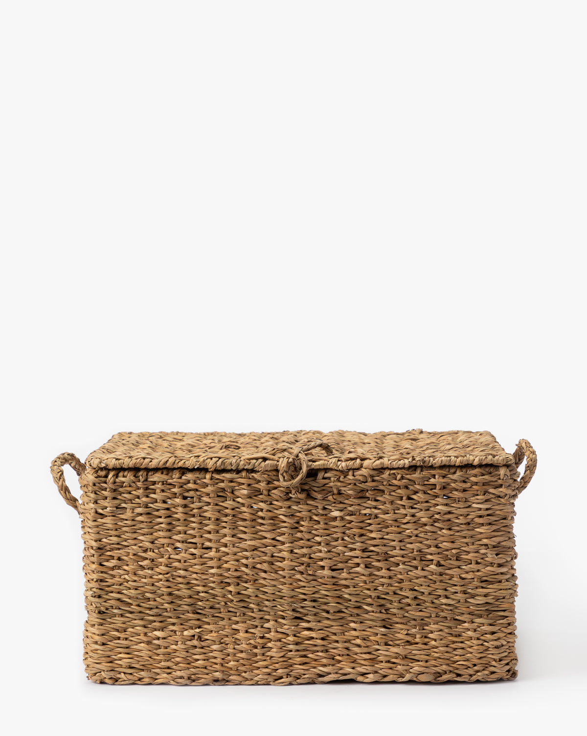 The Kya Seagrass Box is a rectangular, hand-woven storage box with a lid and side handles, crafted from natural light brown seagrass fibers and shown against a plain white background by McGee & Co.