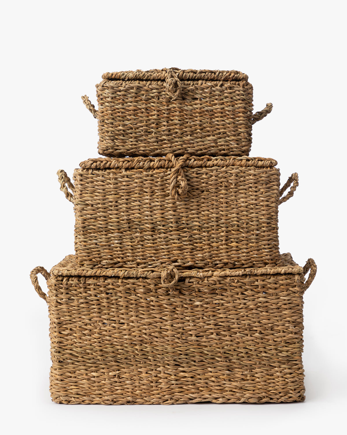 The Kya Seagrass Box set features three rectangular, hand-woven wicker baskets with lids and side handles, stacked from largest to smallest for a charming decorative touch against a plain white background, by McGee & Co.
