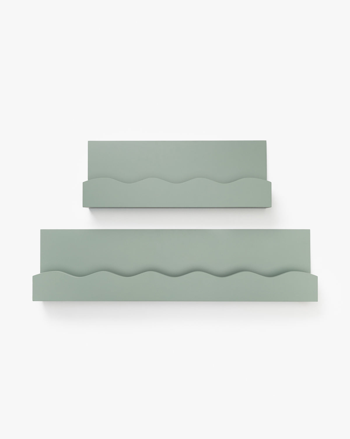 Two sage green Kylee Shelves with wavy front edges are mounted on a white wall. The shelves, ideal for a child’s room, are different sizes—the larger shelf sits slightly below and to the right of the smaller one, by McGee & Co.