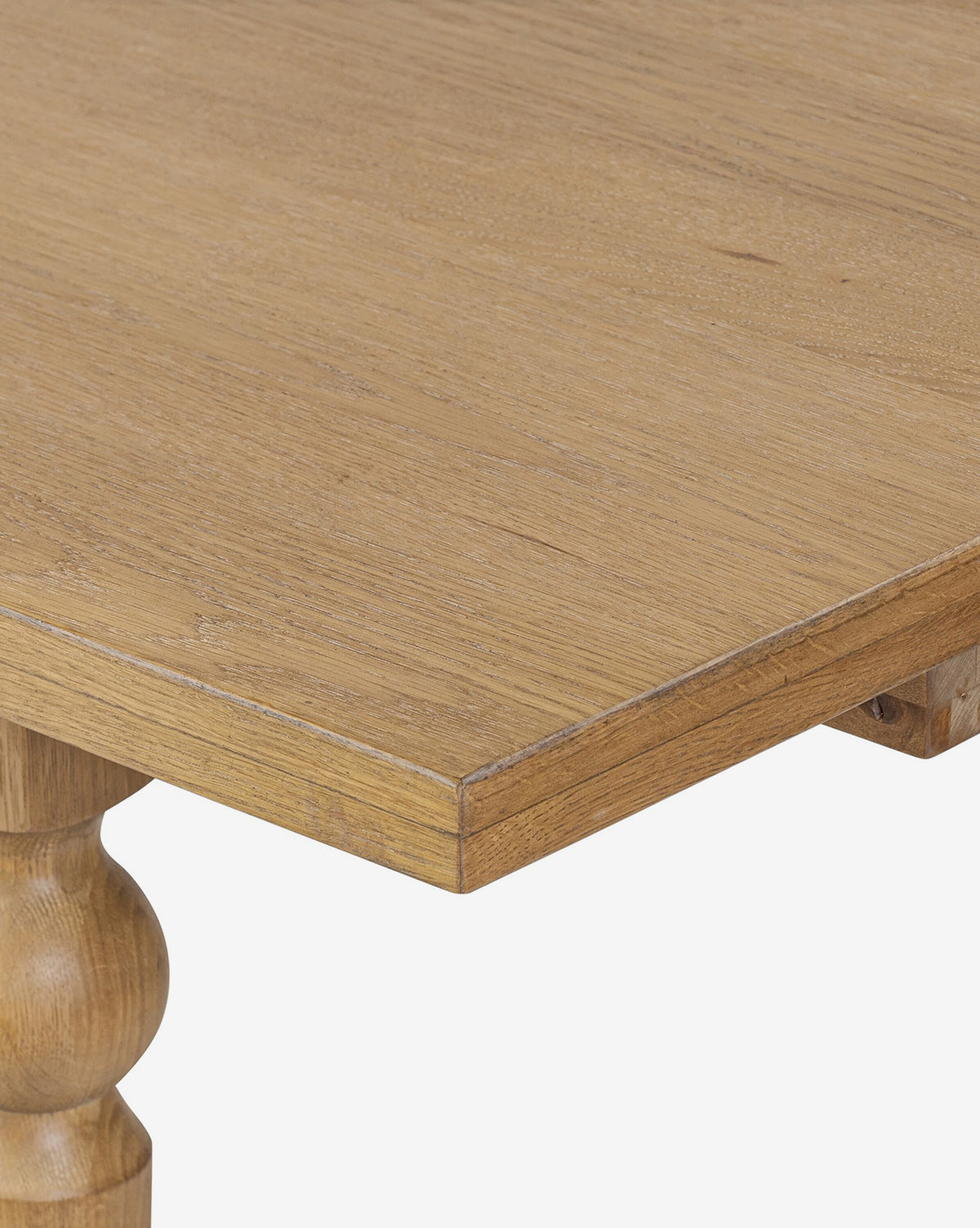 Close-up of the Kyler Oak Extension Dining Table corner, featuring a smooth, light brown surface and a turned leg against a plain white background, by McGee & Co.