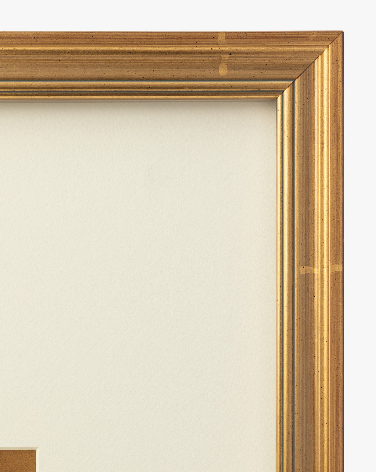 A close-up of the top right corner of the gold-colored wooden Lace Detail frame with an off-white mat inside. Slight wear and a few scratches add vintage charm, making it perfect for wall art and enhancing your home decor, by McGee & Co.