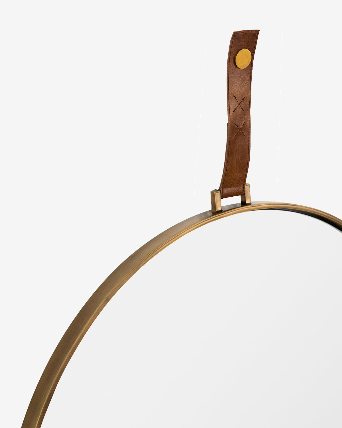 The Laila Circle Mirror features a brass frame and circular design, suspended by a brown stitched leather hanger with a brass fastener, standing out elegantly against a white background, by McGee & Co.