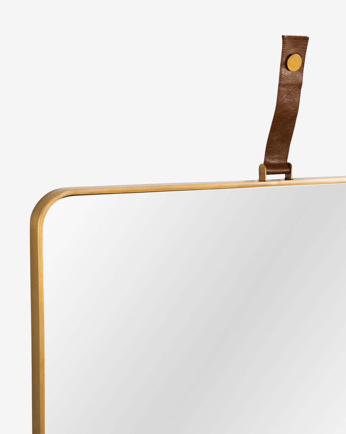 Close-up of the top corner of the Laila Rectangle Mirror, featuring a gold metal frame and brown leather hanger with brass hardware, set against a plain white background, by McGee & Co.