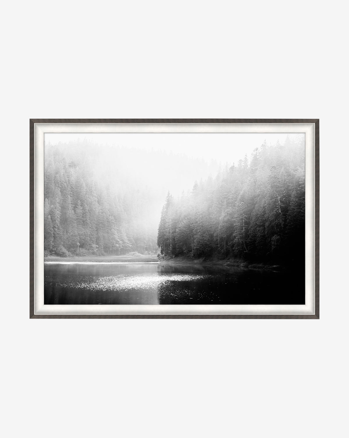 Lakeside is a black and white giclee wall art print featuring a misty forest by a calm lake with sunlight on the water, elegantly framed with a white mat and slim metallic border.