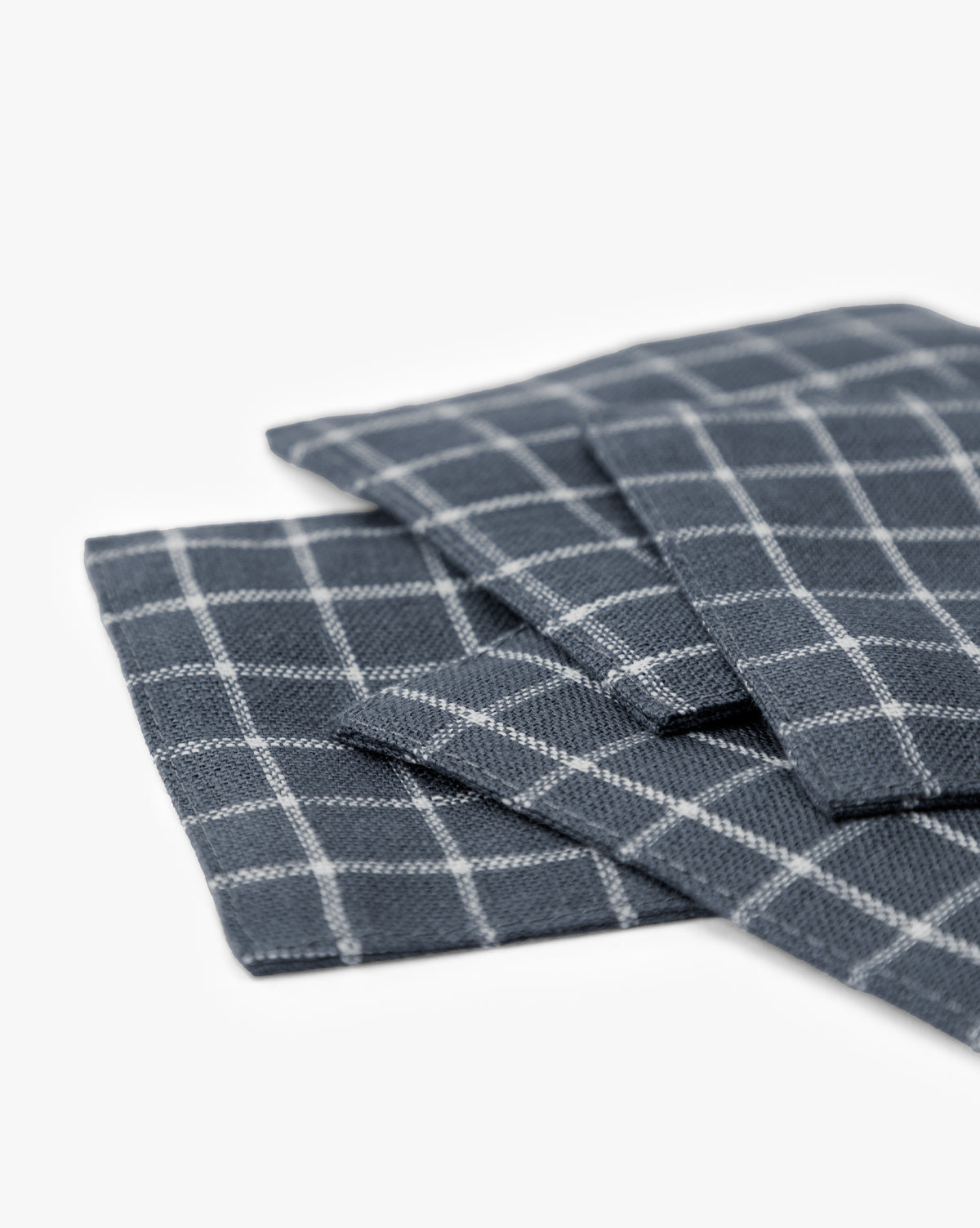 A close-up of Lancaster Linen Coasters (Set of 4) in dark gray with a white checkered pattern, neatly stacked on a white surface—perfect absorbent coasters for stylish table settings, by McGee & Co.