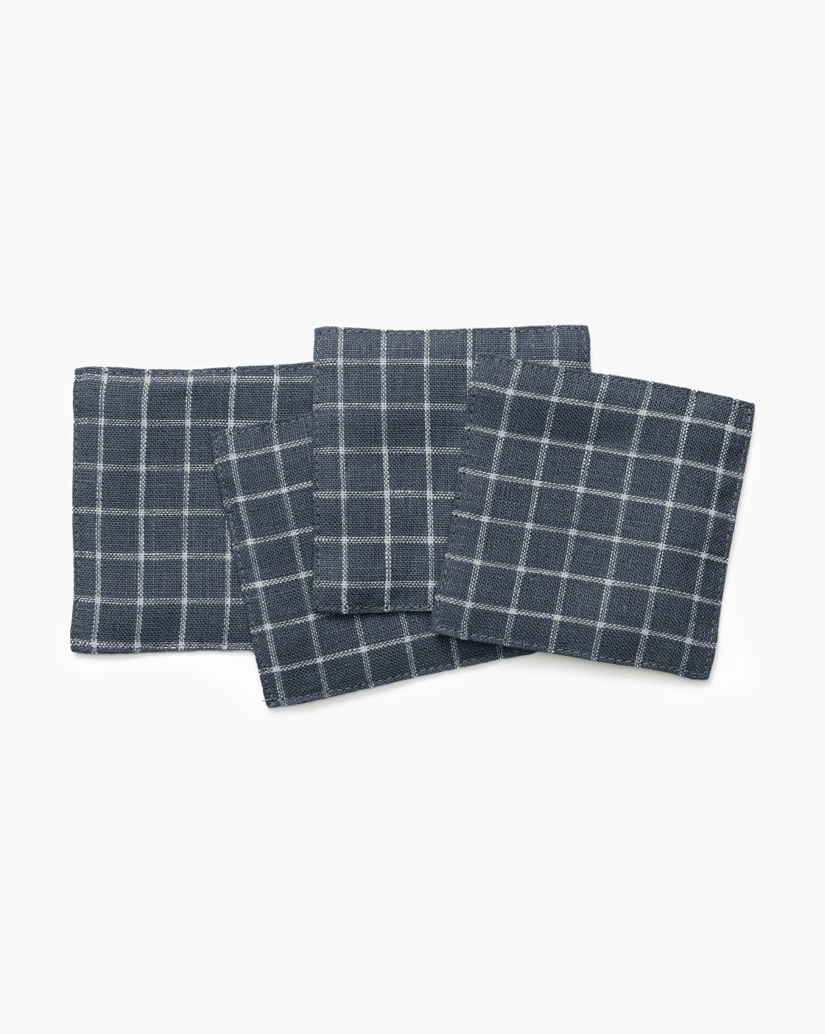 The Lancaster Linen Coaster Set (Set of 4) features dark gray linen coasters with a white grid pattern, arranged with slight overlap on a white background for a stylish and absorbent table solution, by McGee & Co.