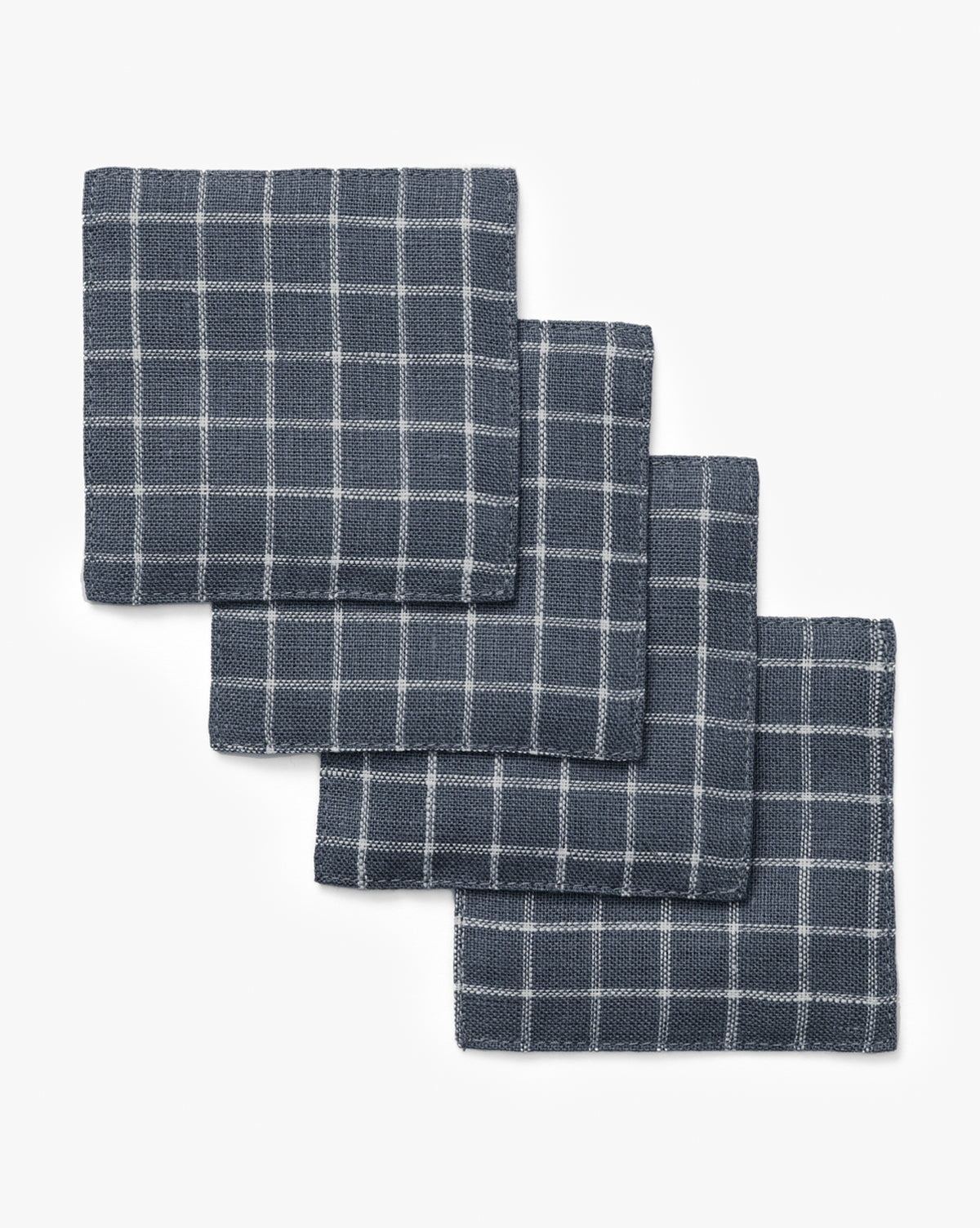 A set of four Lancaster Linen Coasters with a navy blue and white checkered pattern is displayed in a slightly overlapping, diagonal stack on a white background, by McGee & Co.