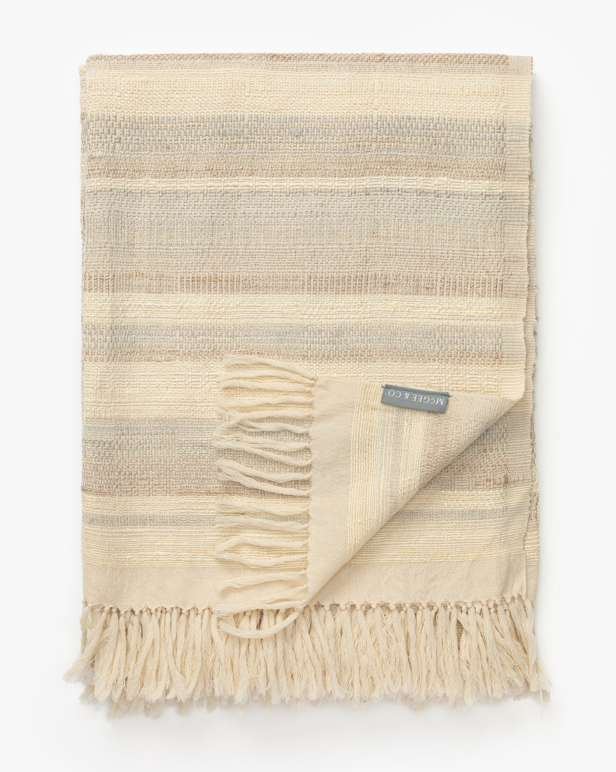 The Laney Stripe Throw by TAL HANDWOVEN CLASSICS LLP features beige and cream woven stripes, fringed edges, and a fabric label—luxuriously displayed on a white background, perfect for elevating any space. McGee & Co.