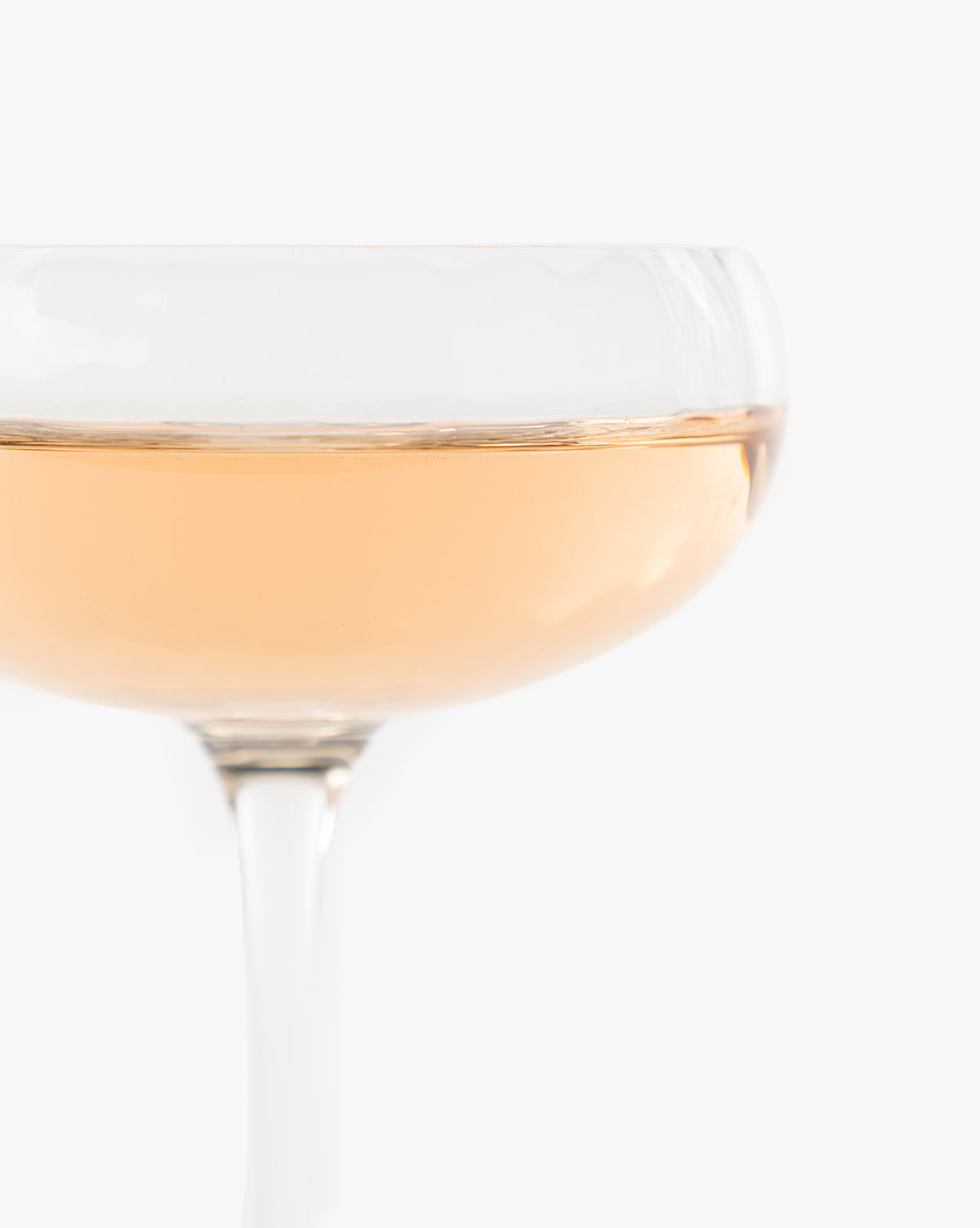 A close-up of the Langford Coupe (Set of 4) filled with pale pink sparkling wine, showing only the upper half of this elegant glassware against a plain white background, by McGee & Co.