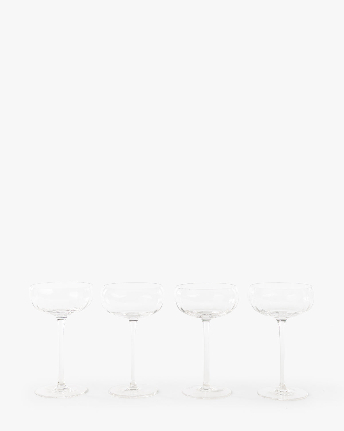 A set of four clear Langford Coupe glasses is evenly spaced in a row against a plain white background, highlighting this elegant glassware perfect for any celebration, by McGee & Co.