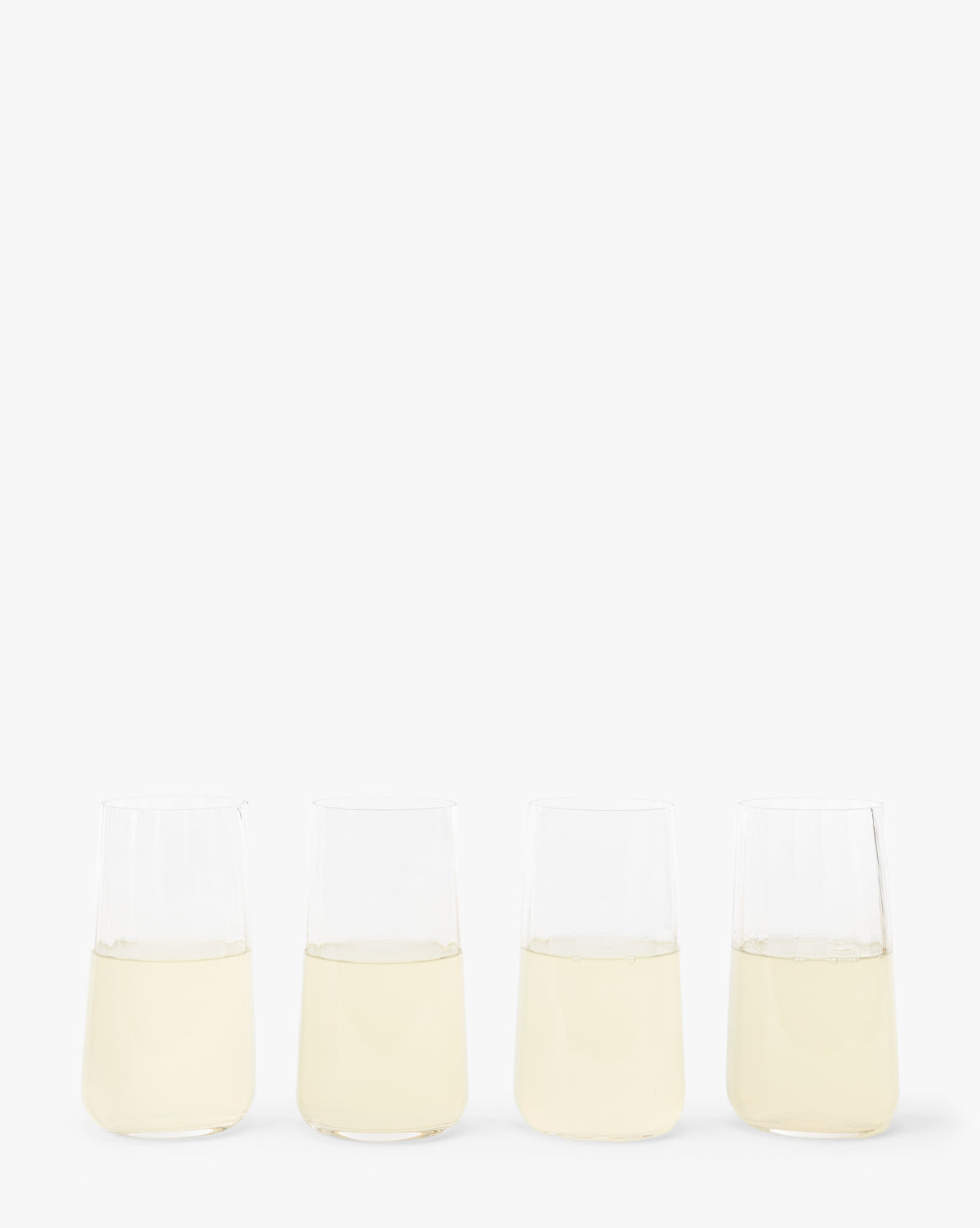 A set of four Langford Highball Glasses, each filled with a light yellow liquid, arranged in a row on a plain white background by McGee & Co.