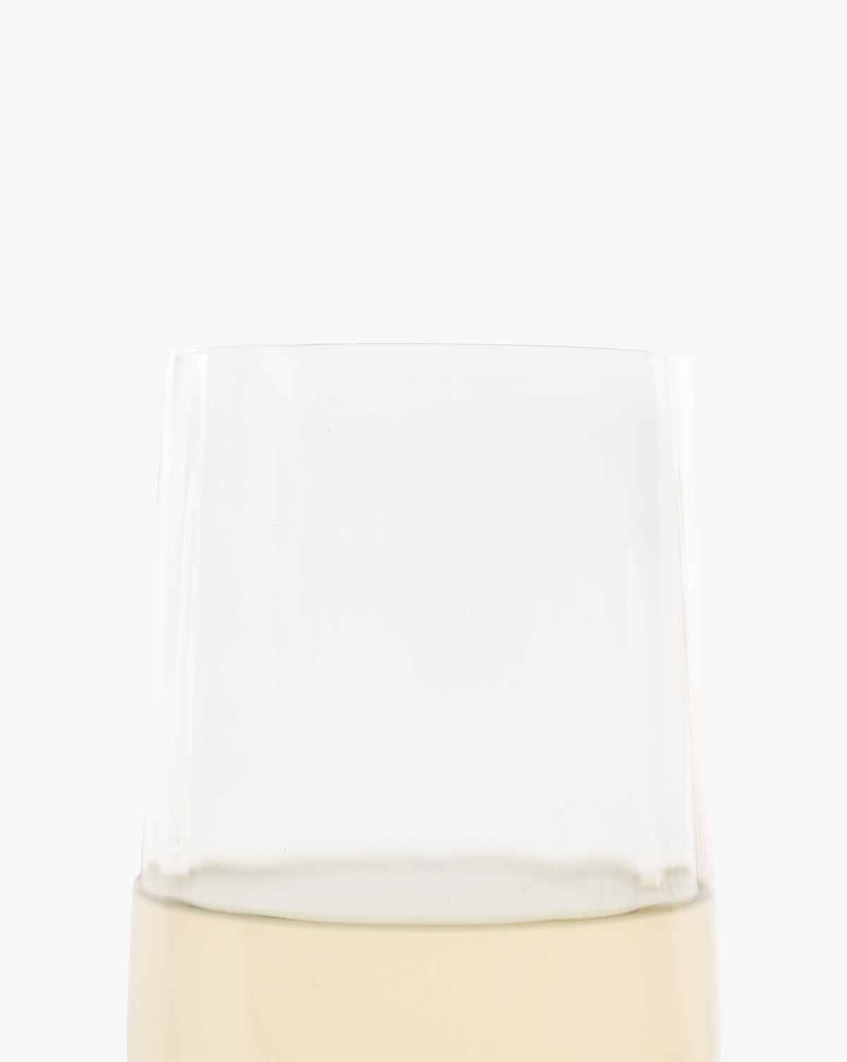 A close-up of the top half of a Langford Highball Glass, filled with pale yellow liquid, set against a plain white background. Only the upper portion of the clear glass is visible by McGee & Co.