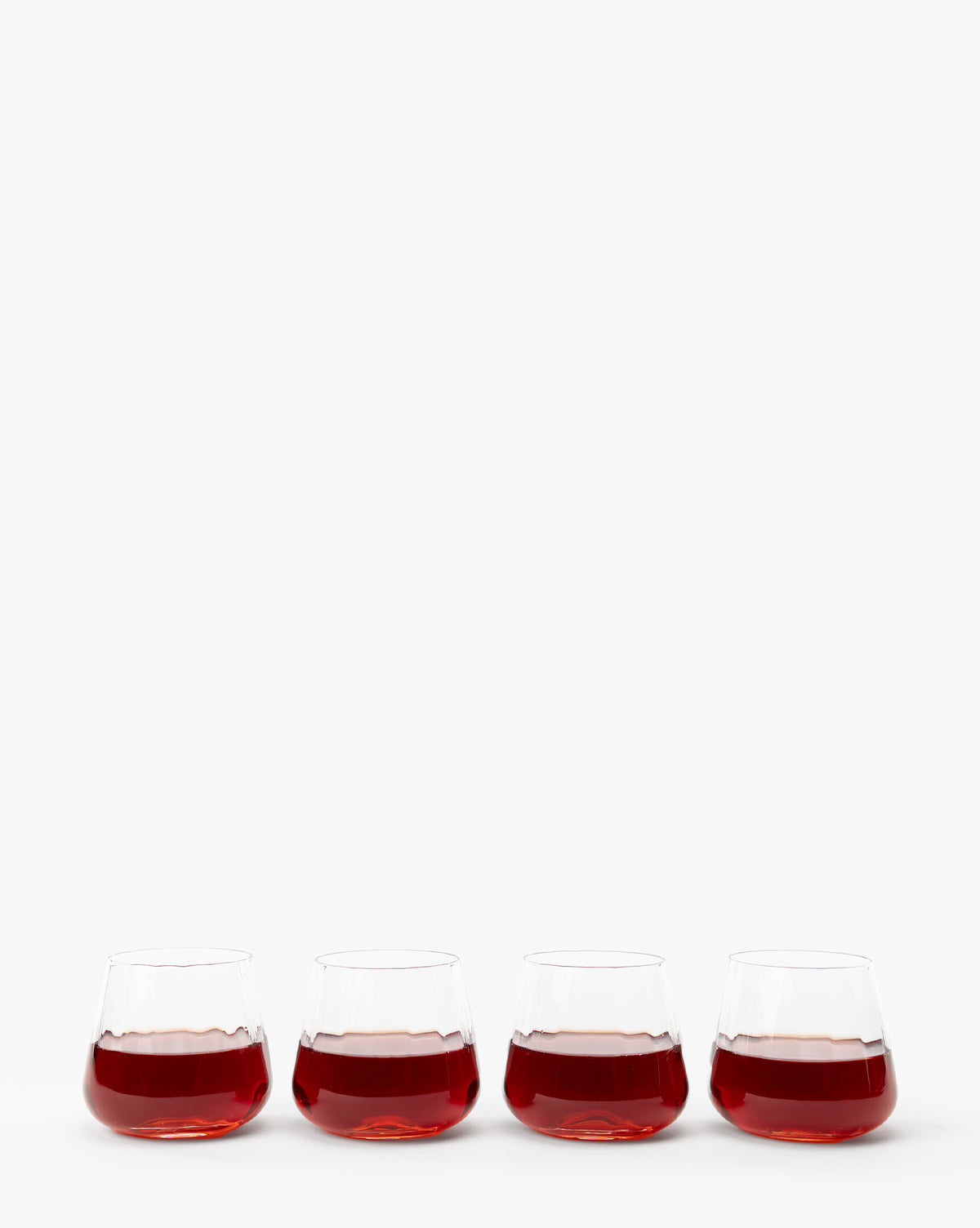 A set of four Langford Tumblers, each filled with red wine, are arranged in a row against a plain white background—an elegant addition to any table setting, by McGee & Co.