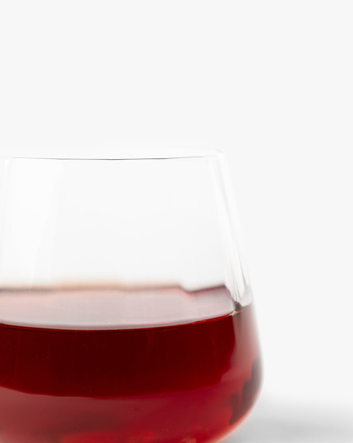 A close-up of a partially filled Langford Tumbler from the Langford Tumblers (Set of 4) highlights the rich red wine color and elegant design against a plain white background, emphasizing refined taste and stylish glassware by McGee & Co.