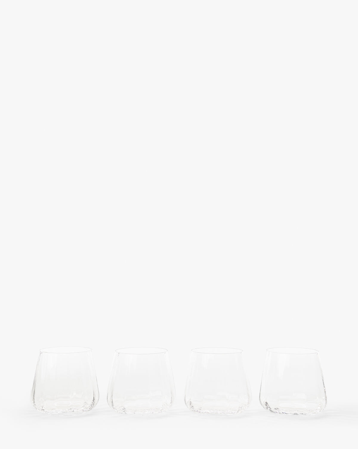 The Langford Tumblers (Set of 4) are arranged in a row on a white surface with a plain white background, providing an elegant glassware choice for any table setting by McGee & Co.