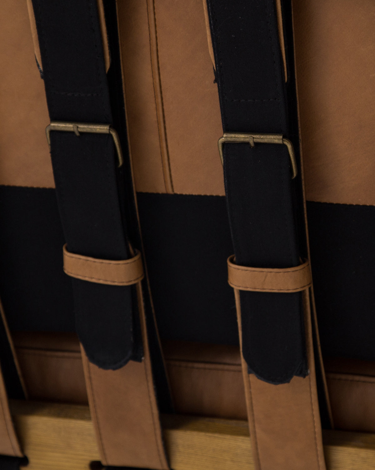 Close-up of three black fabric straps with brown leather accents and brass buckles, attached to a brown and black upholstered surface on the Lanston Lounge Chair with leather cushions by McGee & Co.