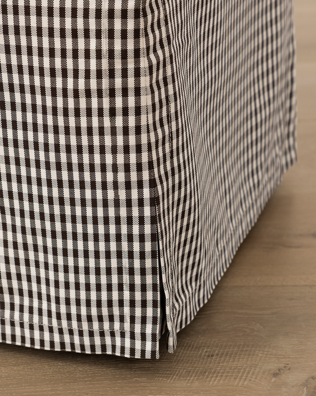 Close-up of the Makerspalm Latimer Ottoman (Ready to Ship), featuring black and white gingham check high-quality fabric, resting on a light wood floor. McGee & Co.