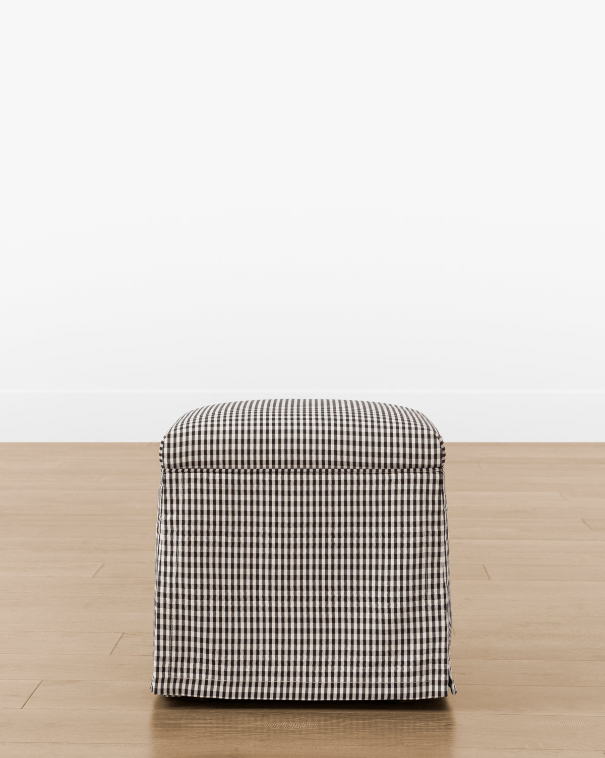 The Makerspalm Latimer Ottoman (Ready to Ship) features a compact square design in premium black and white gingham fabric, shown on a light wood floor with a plain white backdrop—a stylish and practical accent for any room. McGee & Co.