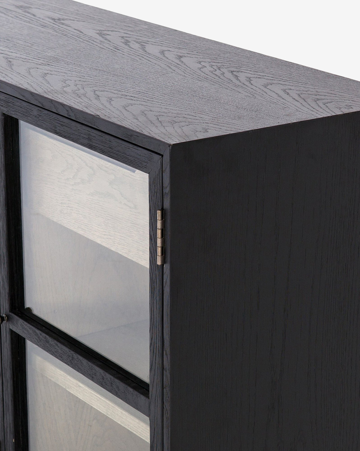 A close-up of the Laura Sideboard’s top corner shows its black wood, glass doors, visible metal hinges, natural drifted finish with wood grain texture, and a glimpse of the interior shelves.