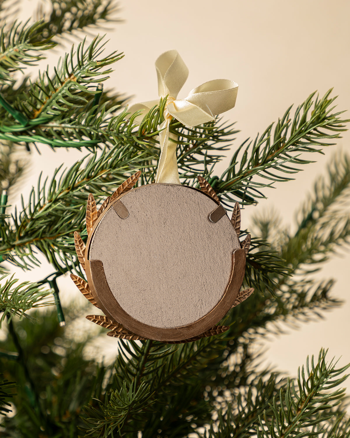 The Laurel Picture Frame Ornament is a round, blank wooden frame with a gold border and cream ribbon, hanging from a green Christmas tree—perfect as a holiday ornament or sentimental gift, by McGee & Co.