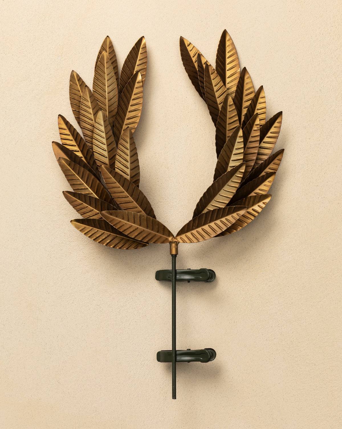 The Laurel Tree Topper, featuring bronze-colored metallic leaves and a golden finish, is mounted on a beige wall with two dark clamps and a central rod, by McGee & Co.
