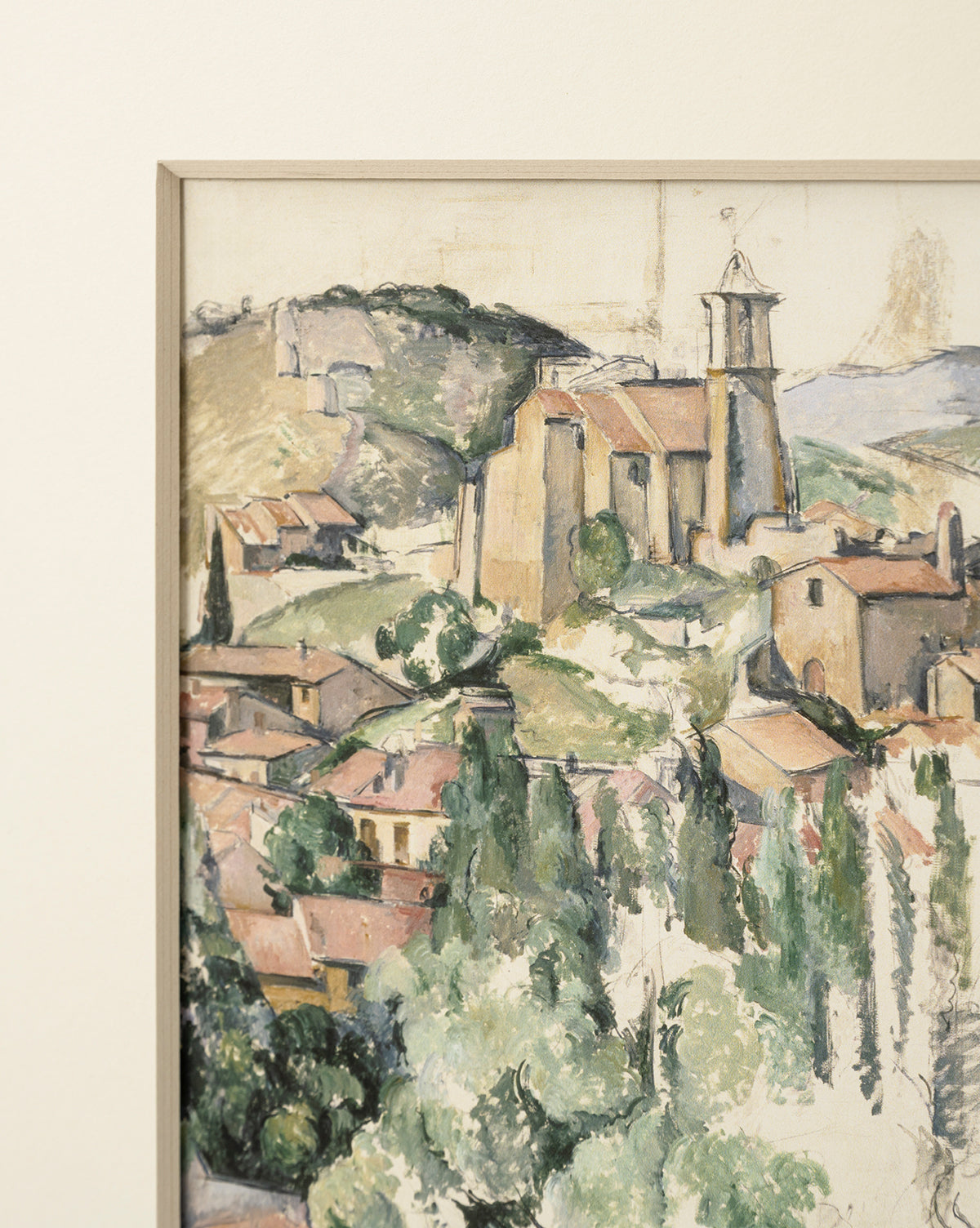 Le Village, a giclee print of a painted landscape, features a hillside village with a stone church and red-roofed houses among green hills and trees under a light sky, presented in a natural woodgrain frame, by McGee & Co.