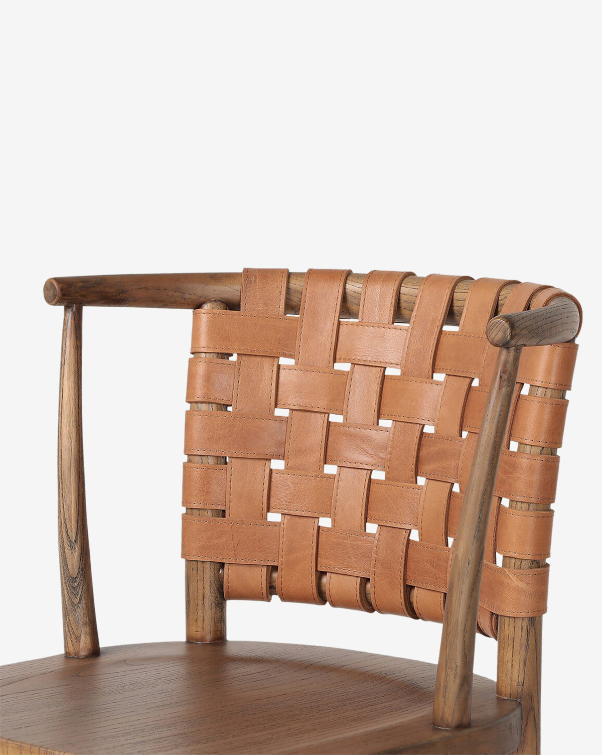 The Lennon Dining Chair features a compact wooden frame, rounded smooth arms, and a woven crisscross backrest made of tan leather straps, complemented by a sturdy wooden seat, by McGee & Co.