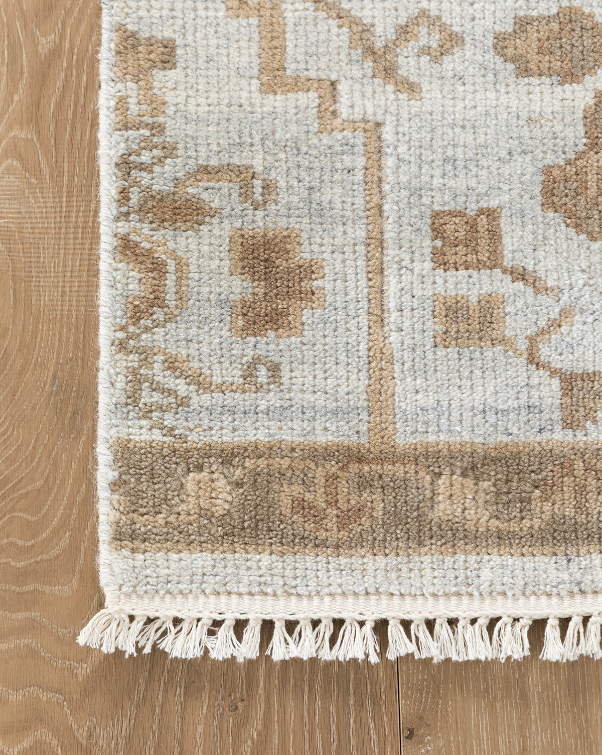 A close-up of the Lexington Hand-Knotted Wool Rug shows its textured wool in beige, brown, and gray tones with fringe edging. This artisan-crafted rug is displayed on a light wood floor, by McGee & Co.