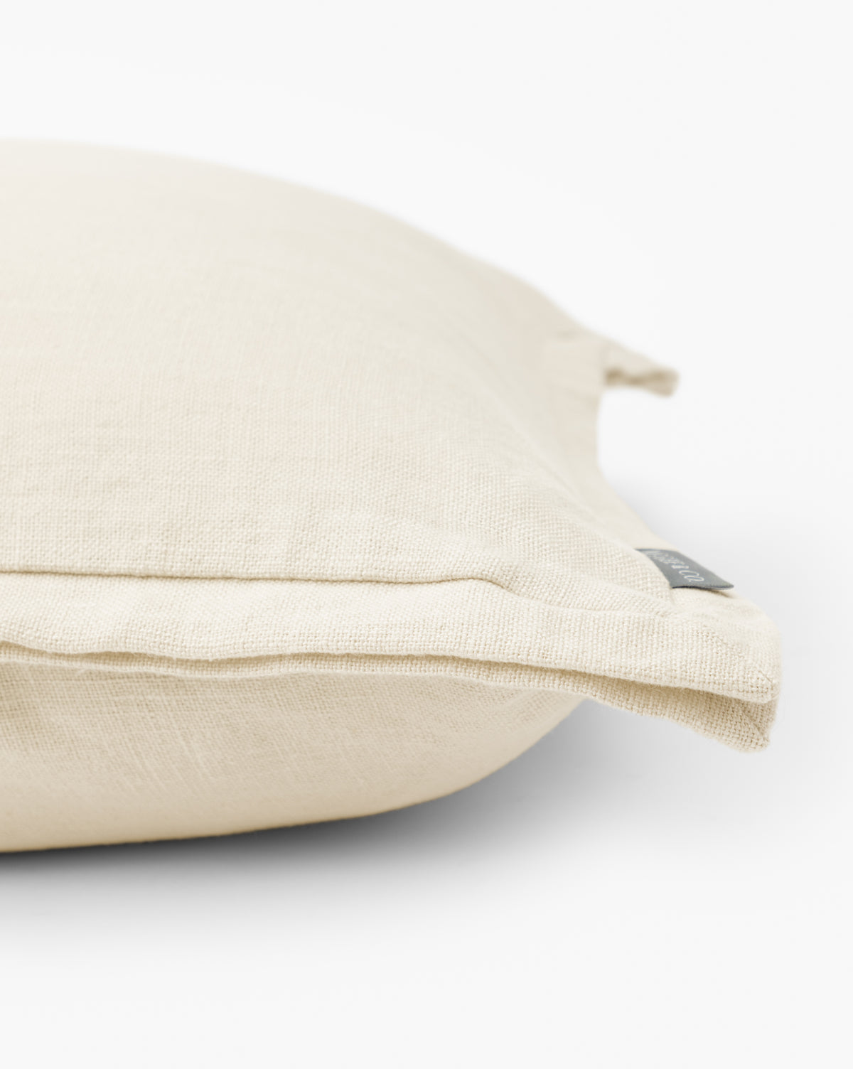 A close-up of the Liam Double Flange Pillow Cover in beige linen, showing its textured fabric and visible seam tag as it rests on a white surface by McGee & Co.