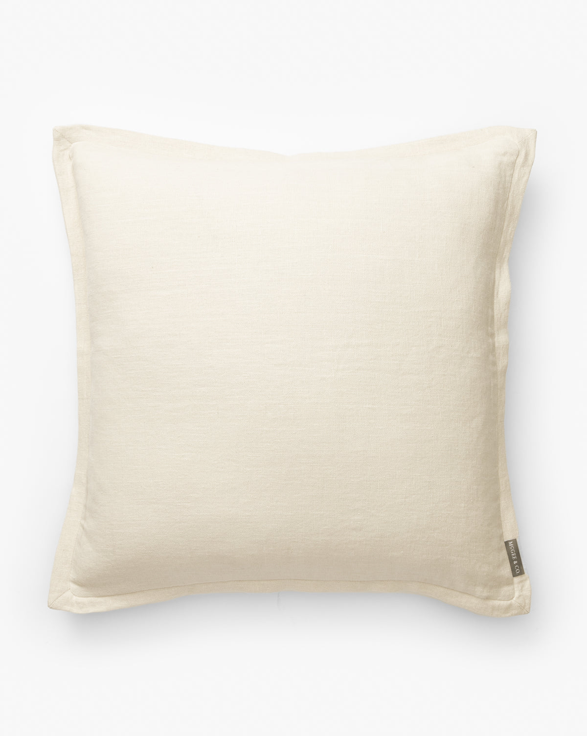 The Liam Double Flange Pillow Cover is a square, off-white decorative cover with a simple design, subtle fabric texture, and refined linen finish. It features a small fabric tag on one edge and is displayed against a plain white background, by McGee & Co.