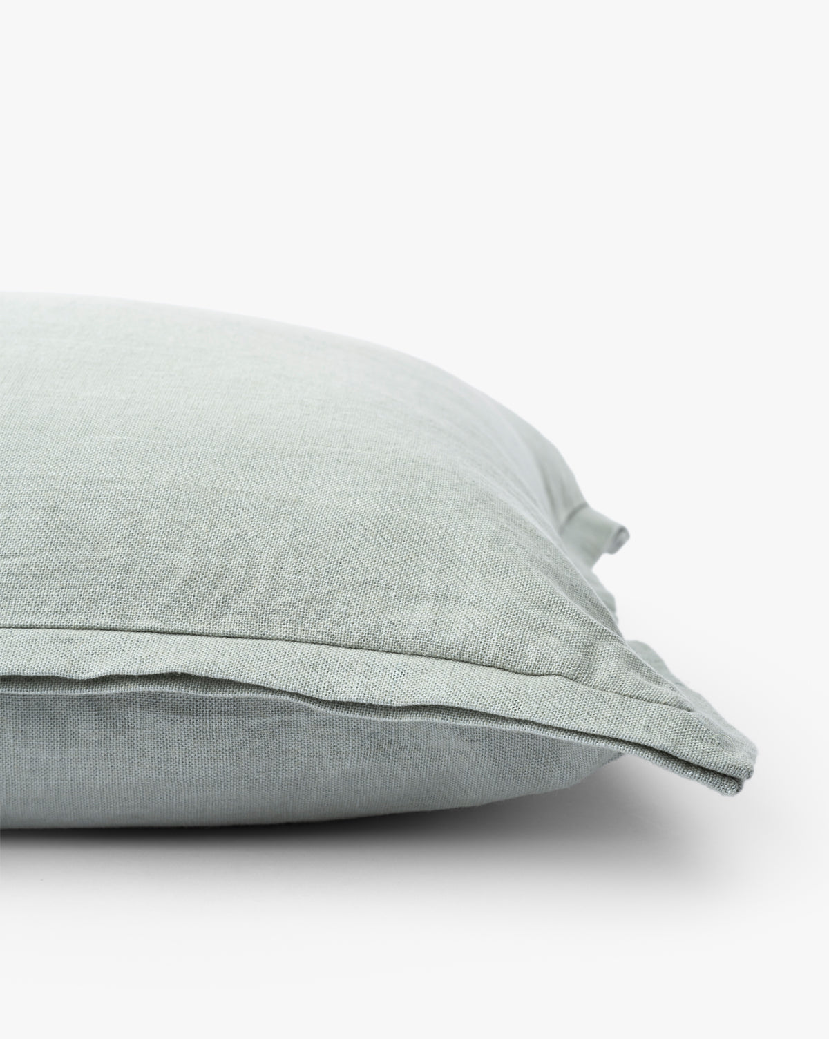 A close-up side view of the Liam Double Flange Pillow Cover in light grayish-green linen shows its soft texture and clean, simple edges against a plain white background, by McGee & Co.