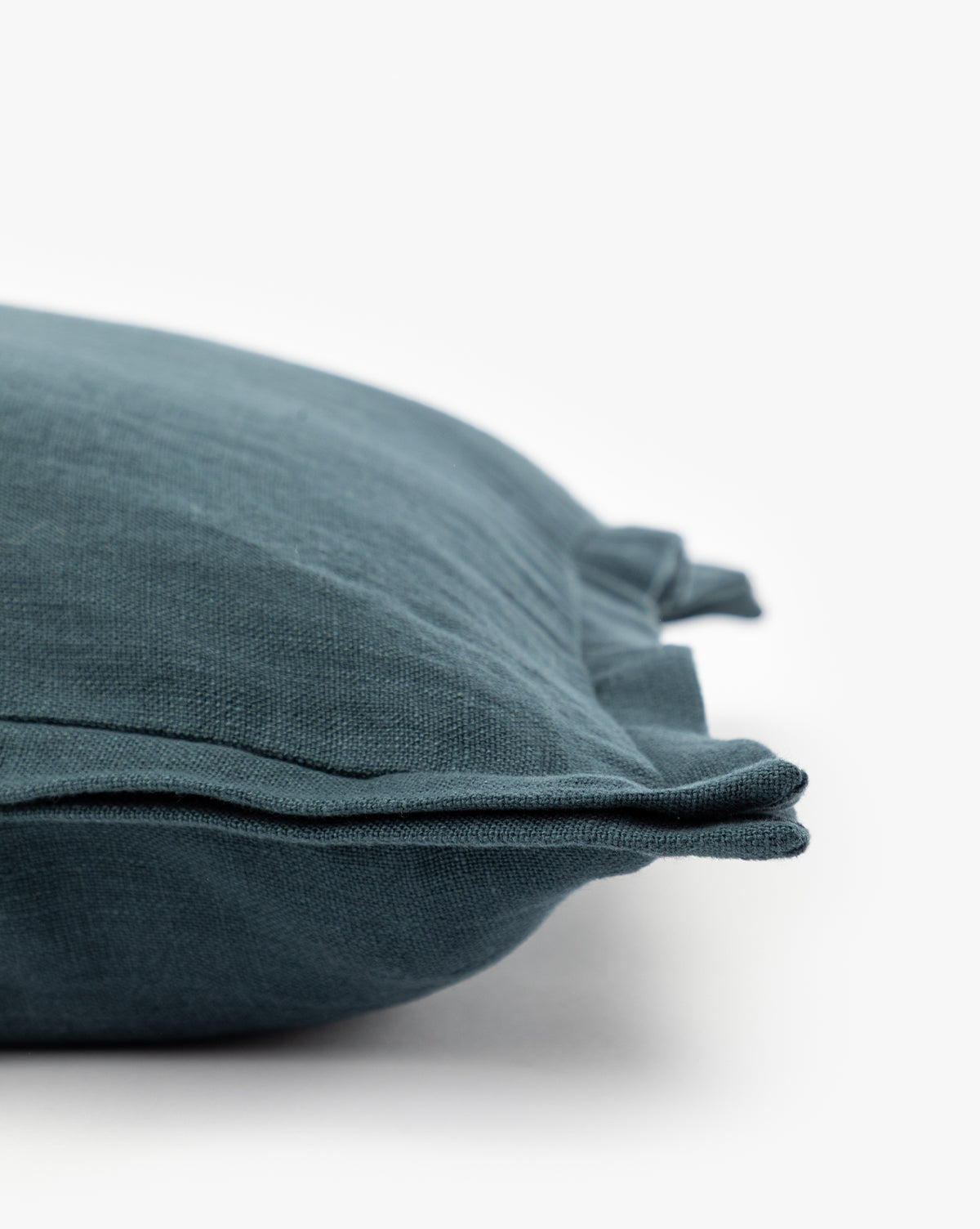 Close-up of the Liam Double Flange Pillow Cover in dark teal, featuring layered double flange edges. Part of the linen cover is shown against a white background, highlighting its texture and fabric details by McGee & Co.