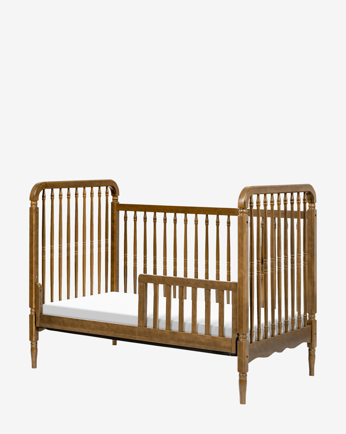 The Liberty 3-in-1 Convertible Spindle Crib with Toddler Bed Conversion Kit features vertical slats, partial safety rail, rounded edges, and decorative posts—shown here as a toddler bed with a white mattress, ideal for your childs transition, by McGee & Co.