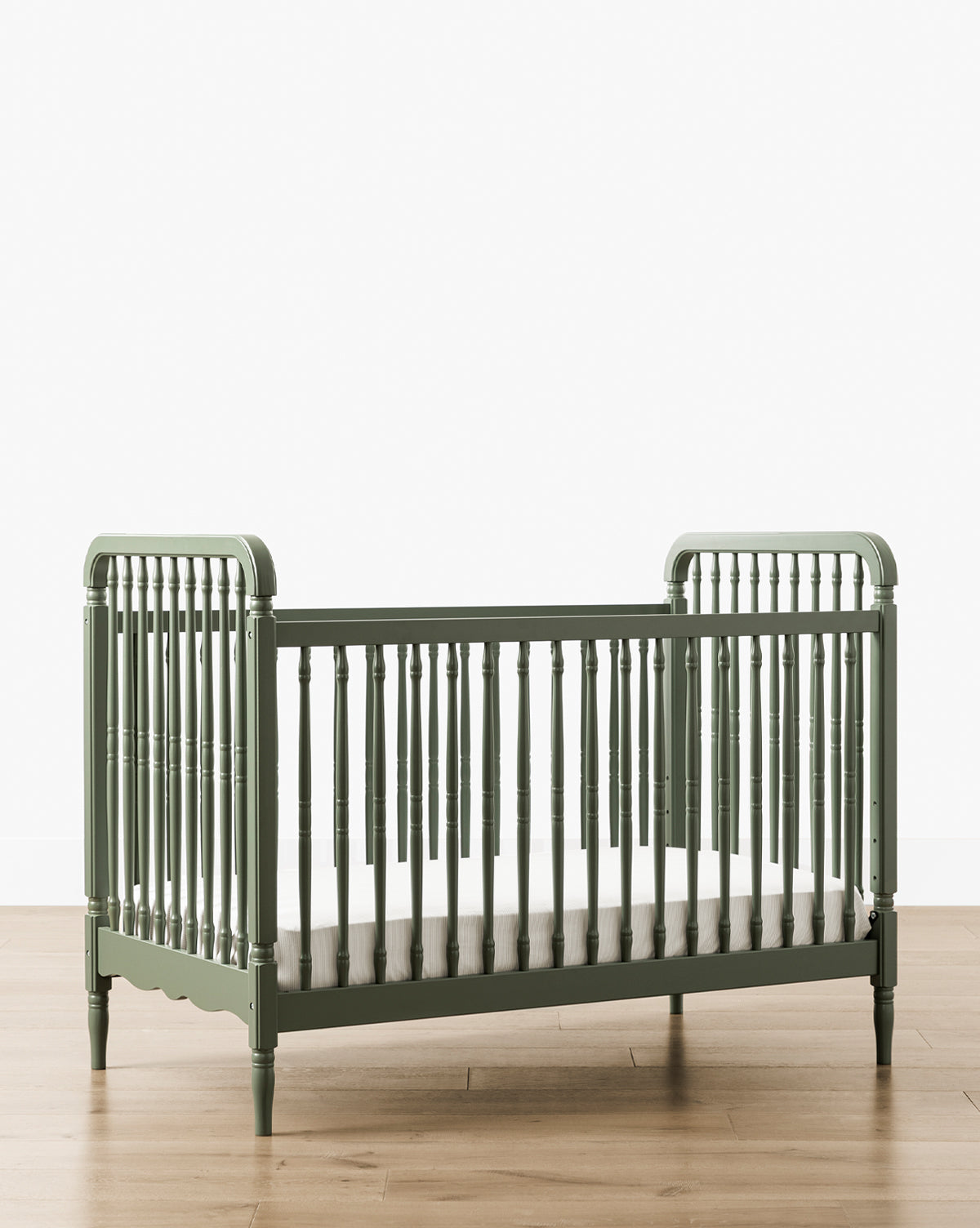 The Liberty 3-in-1 Convertible Spindle Crib w/Toddler Bed Conversion Kit, in green solid pine, with spindled sides and ends, is displayed on a light wood floor against a plain white background by McGee & Co.