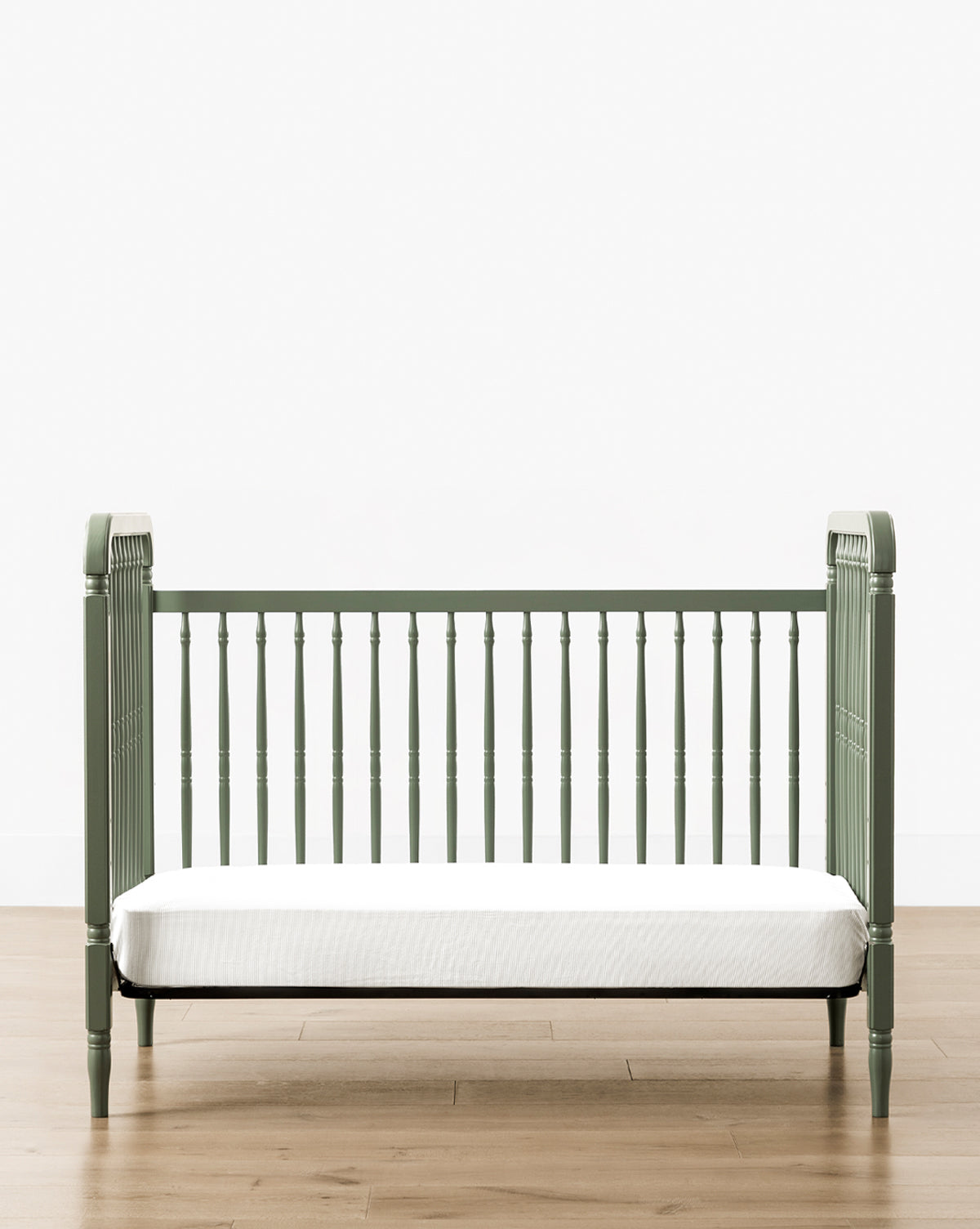 The Liberty 3-in-1 Convertible Spindle Crib comes in green with a white mattress, crafted from solid pine, and includes a Toddler Bed Conversion Kit to adapt as your child grows, by McGee & Co.