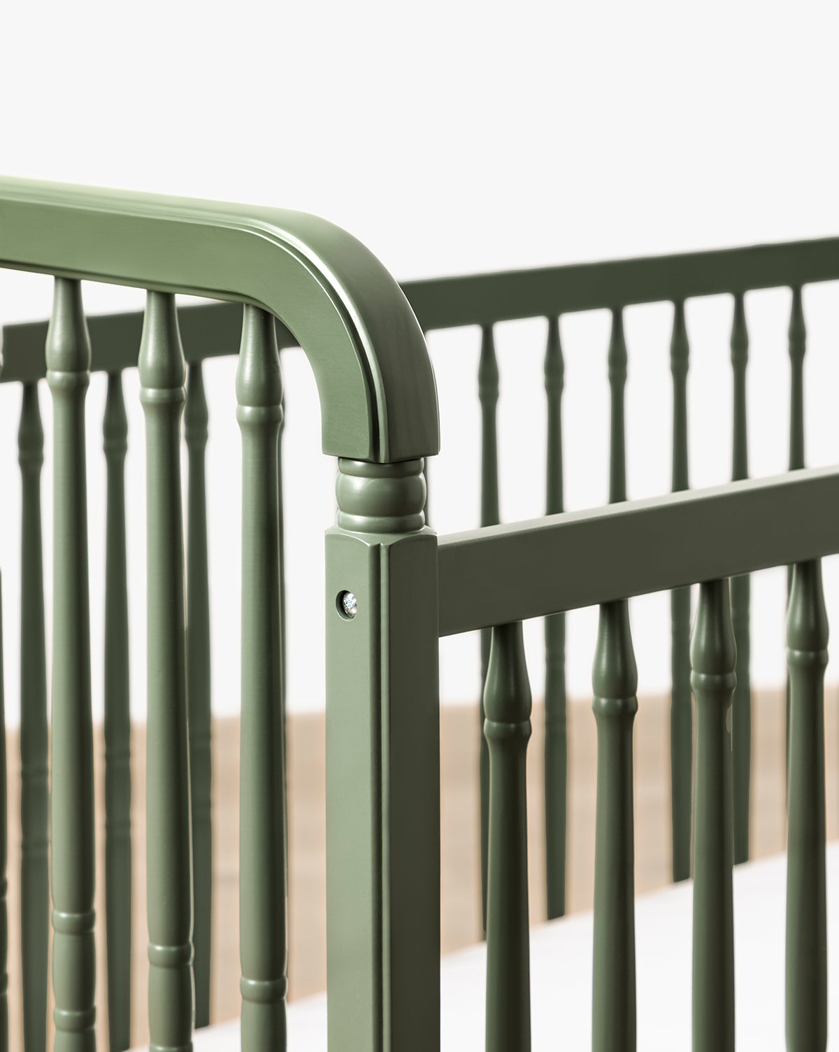 Close-up of the Liberty 3-in-1 Convertible Spindle Crib w/Toddler Bed Conversion Kit, shown in green solid pine with vertical slats and rounded edges, set against a plain light background by McGee & Co.
