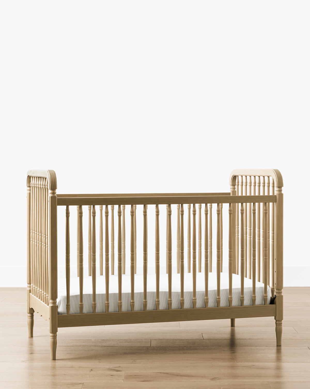 The Liberty 3-in-1 Convertible Spindle Crib w/Toddler Bed Conversion Kit, made of solid pine wood with vertical spindles and rounded corners, sits on a wooden floor against a plain white background and includes a thin mattress inside by McGee & Co.