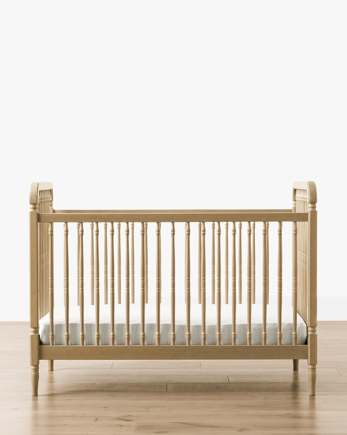 The Liberty 3-in-1 Convertible Spindle Crib with Toddler Bed Conversion Kit, crafted from solid pine wood with vertical slats and a white mattress, is shown on a wooden floor against a plain white background by McGee & Co.