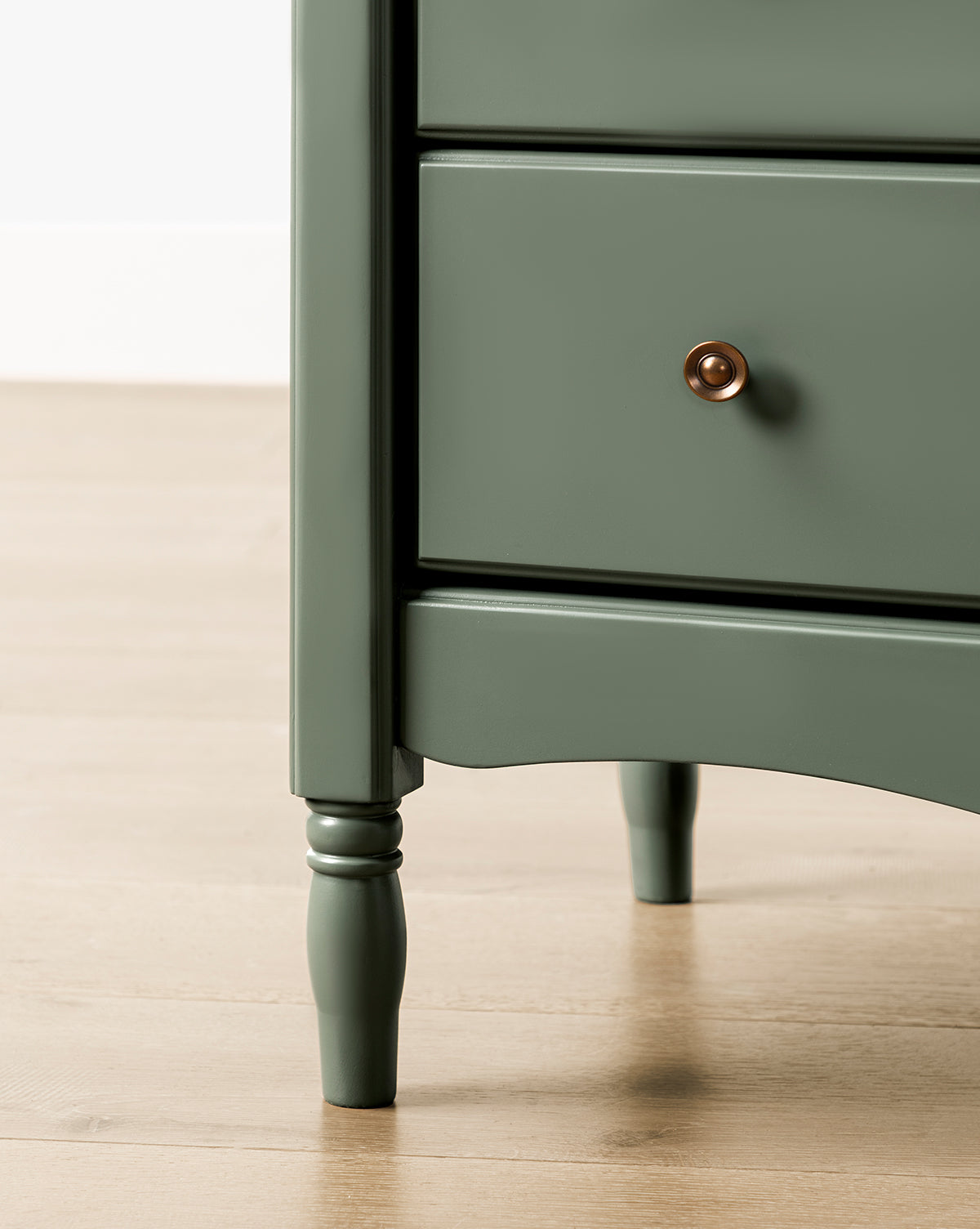 Close-up of the Liberty 6-Drawer Assembled Dresser made from sustainable pine, featuring turned legs, two drawers with round brass knobs, set on a light wood floor against a white wall, by McGee & Co.
