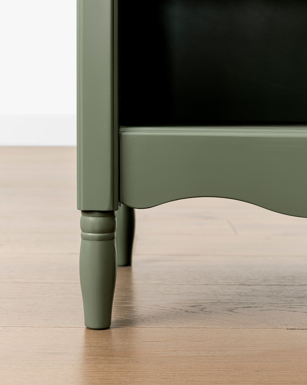Close-up of the bottom corner of the green Liberty Bookcase with turned legs, highlighting heirloom craftsmanship, on a light wood floor against a white wall, by McGee & Co.